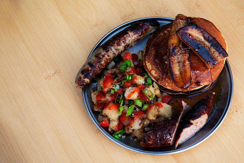 A Titanium Plate on a Single Action Table filled with sausage, hash browns, and sourdough pancakes topped with caramelized bananas.