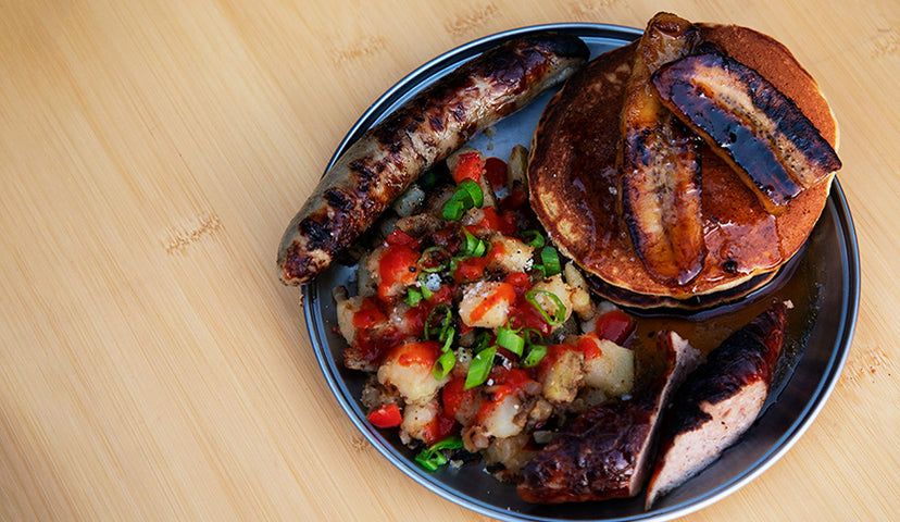 A Titanium Plate on a Single Action Table filled with sausage, hash browns, and sourdough pancakes topped with caramelized bananas.