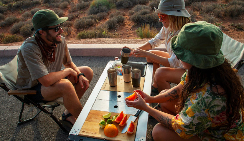 Three friends sit around an Entry IGT Table while preparing Michelada drinks using Snow Peak camping gear.