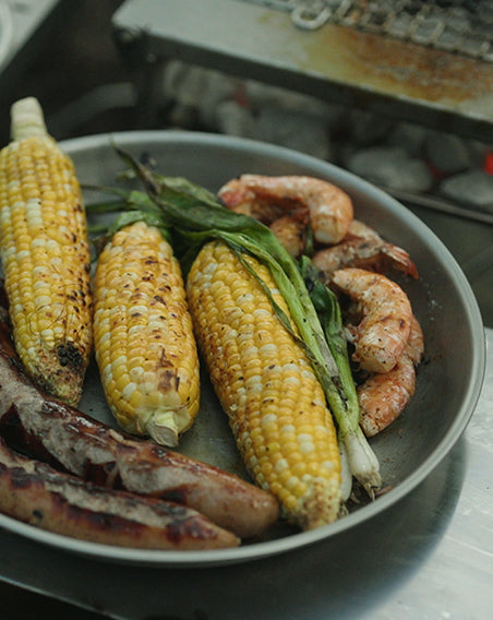 A delicious Snow Peak Titanium Plate of grilled corn, shrimp, and sausages.